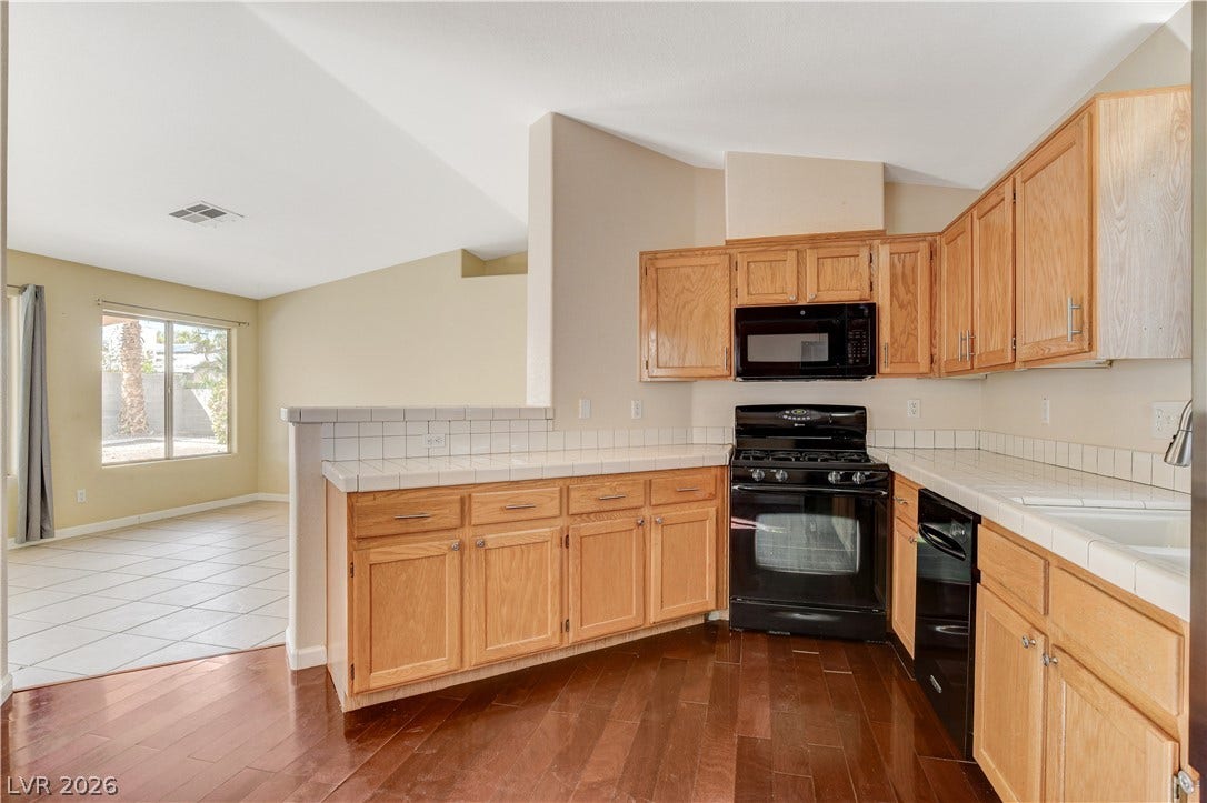 5239 Ferrell Mountain Court, North Las Vegas, NV 89031 Rich wood flooring runs through this kitchen featuring tile countertops and classic oak cabinetry.