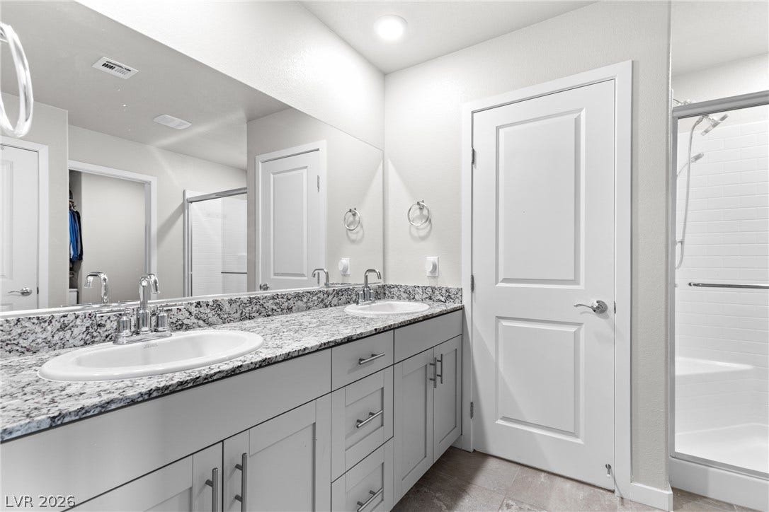 A spacious double vanity features granite countertops alongside a modern glass-enclosed shower.