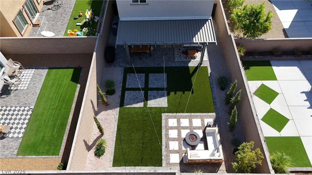 An organized outdoor space combines a covered patio, geometric turf patterns, and a cozy fire pit.