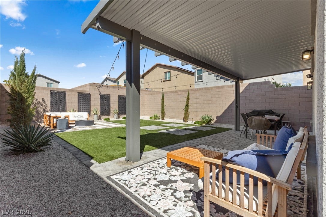 A sheltered patio opens to a low-maintenance backyard enclosed by block walls under clear skies.