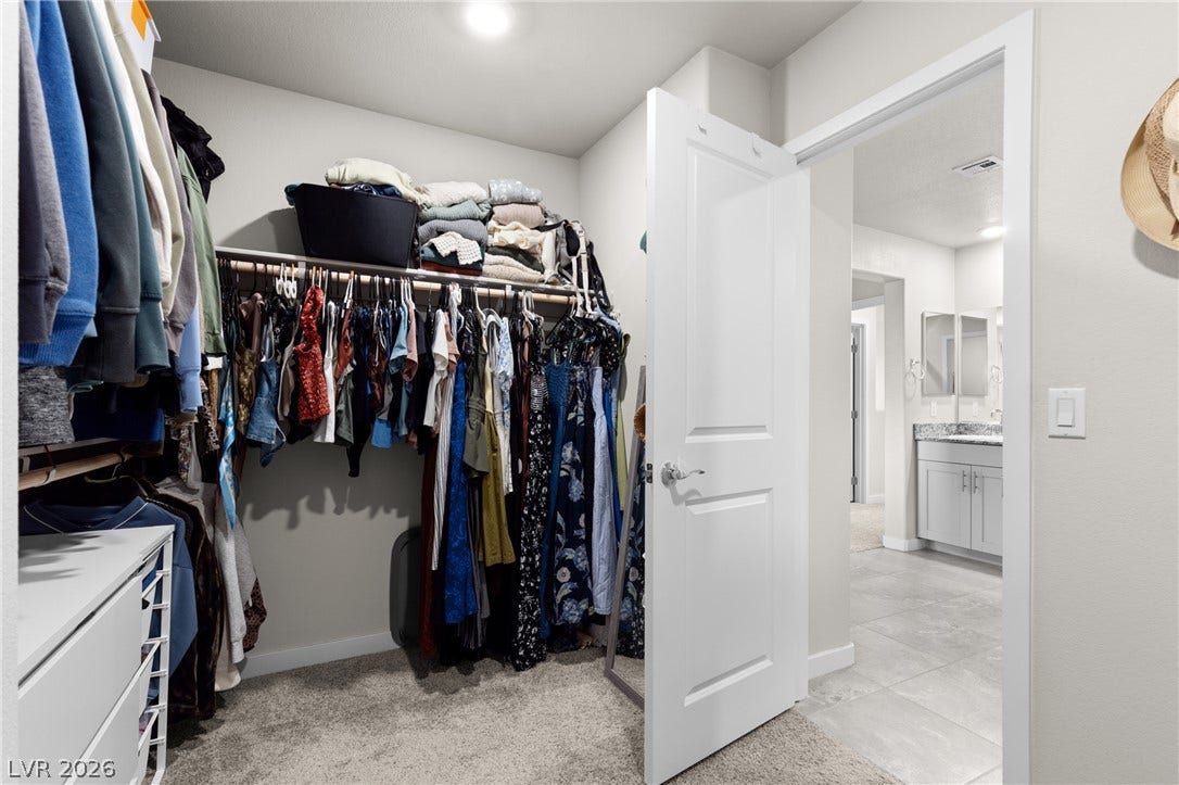 A spacious walk-in closet includes ample hanging rods and direct access to the adjacent bathroom.