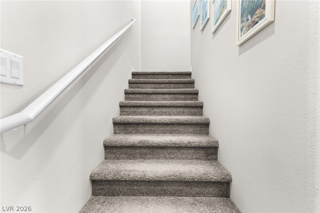 Plush carpeted stairs ascend between clean-lined walls equipped with a functional handrail.