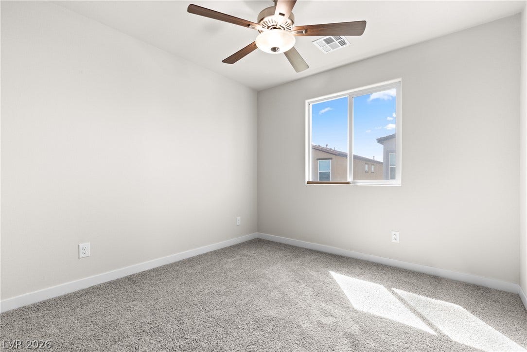 Natural light pours through a large window onto soft carpeting in this comfortable bedroom.