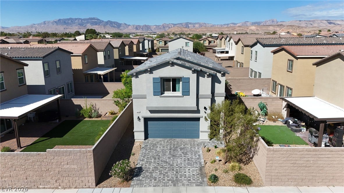 A paved driveway leads to a modern two-story home backed by sweeping mountain views.