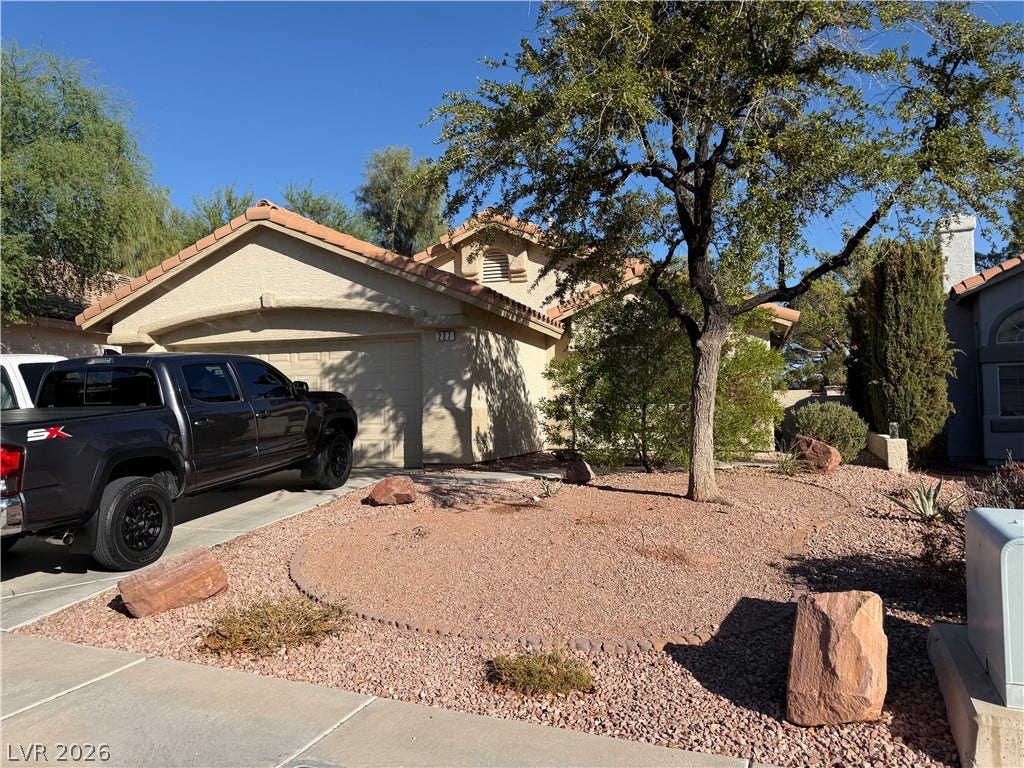 227 Camelback Ridge Avenue, Henderson, NV 89012 Desert landscaping and a concrete driveway lead to the tiled-roof garage of this stucco home.