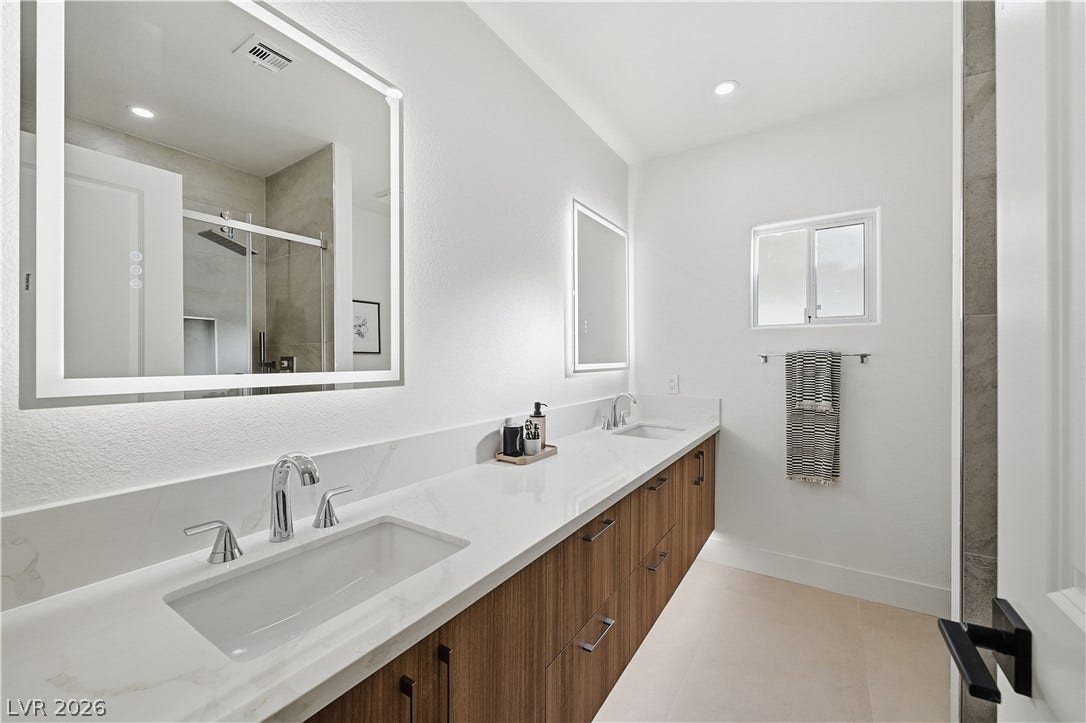 1612 Hidden Spring Drive, Las Vegas, NV 89117 A long stone double vanity with modern wood cabinets anchors this bright master bathroom.