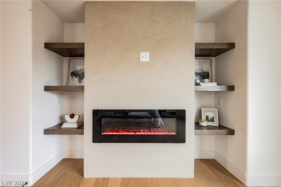 A modern linear fireplace anchors the room, flanked by floating wood display shelves.