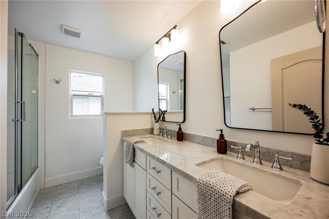 A spacious double vanity features elegant stone countertops and a modern glass-enclosed shower.