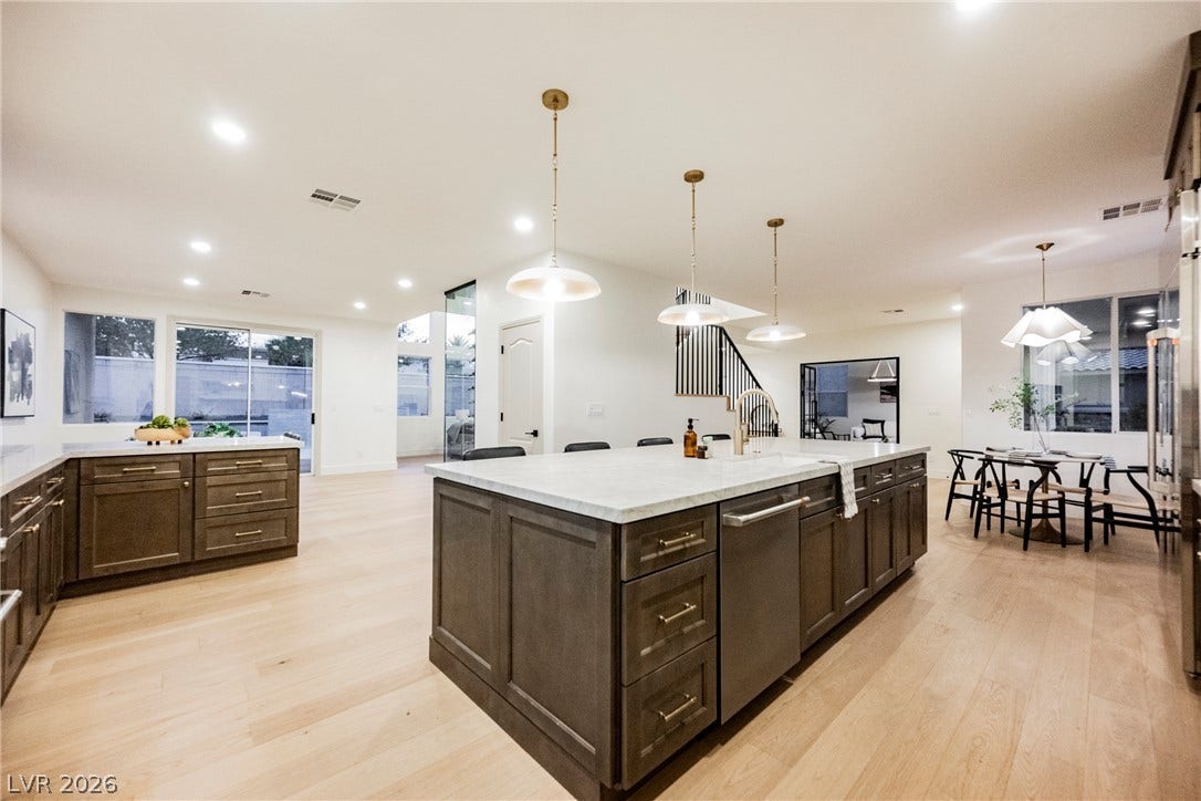 Crisp recessed lighting illuminates a spacious kitchen with warm wood flooring and clean architectural lines.