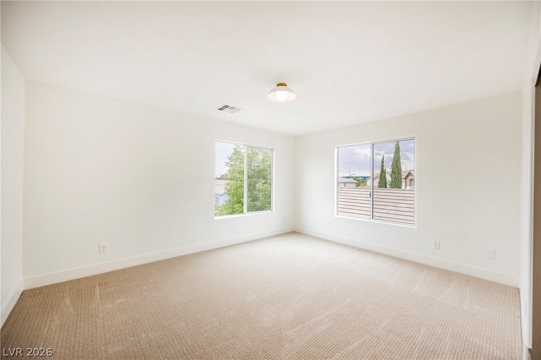 Dual windows frame leafy neighborhood views in this light-filled bedroom with plush textured carpeting.