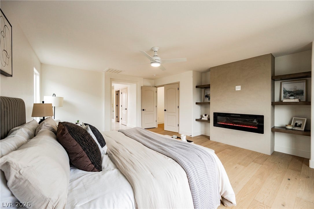 A modern fireplace and warm wood flooring anchor this serene primary bedroom retreat.