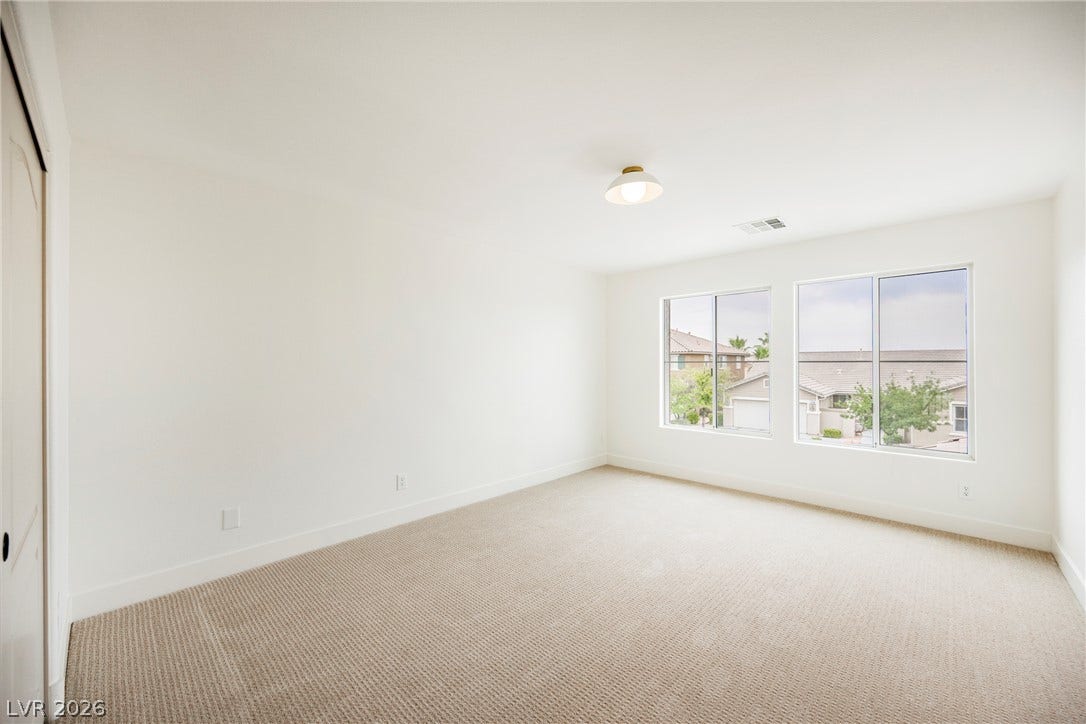 A spacious bedroom features plush neutral carpeting and large windows overlooking the neighborhood.