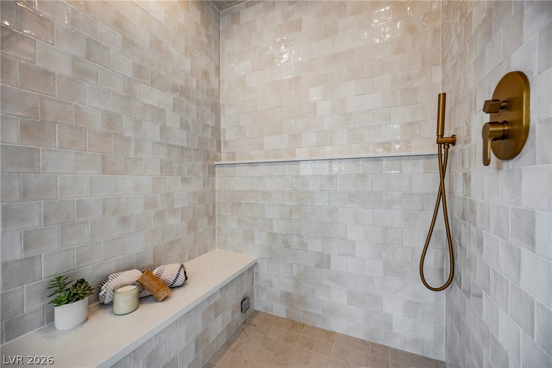 Gleaming wall-to-wall tiling and modern gold fixtures elevate this walk-in shower space.