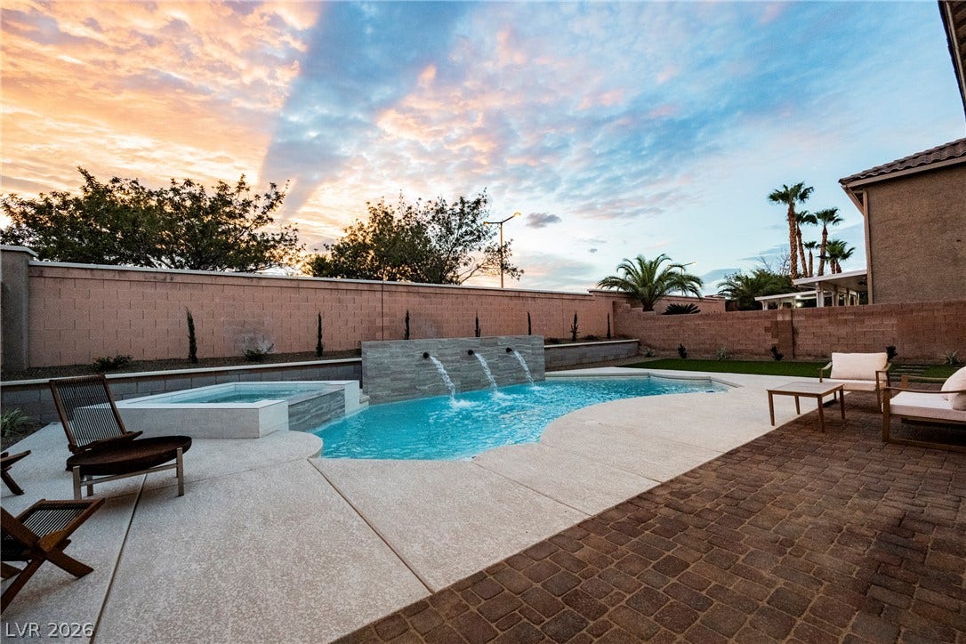 An inviting backyard oasis showcases a custom swimming pool paired with a spilling spa.