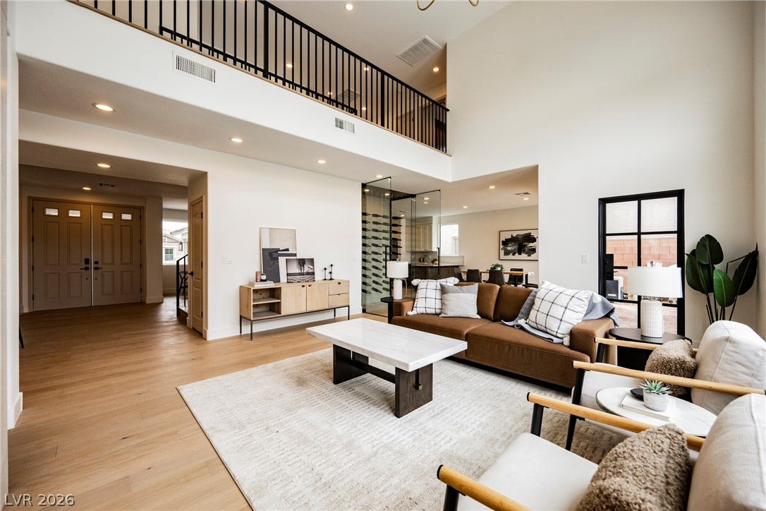 Sunlight streams across the wood floors of this double-height living room featuring an upper overlook.