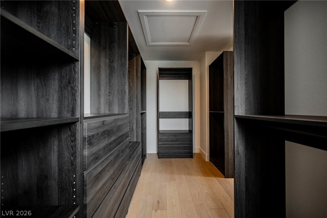 Custom dark wood cabinetry lines this spacious walk-in closet featuring light hardwood floors.
