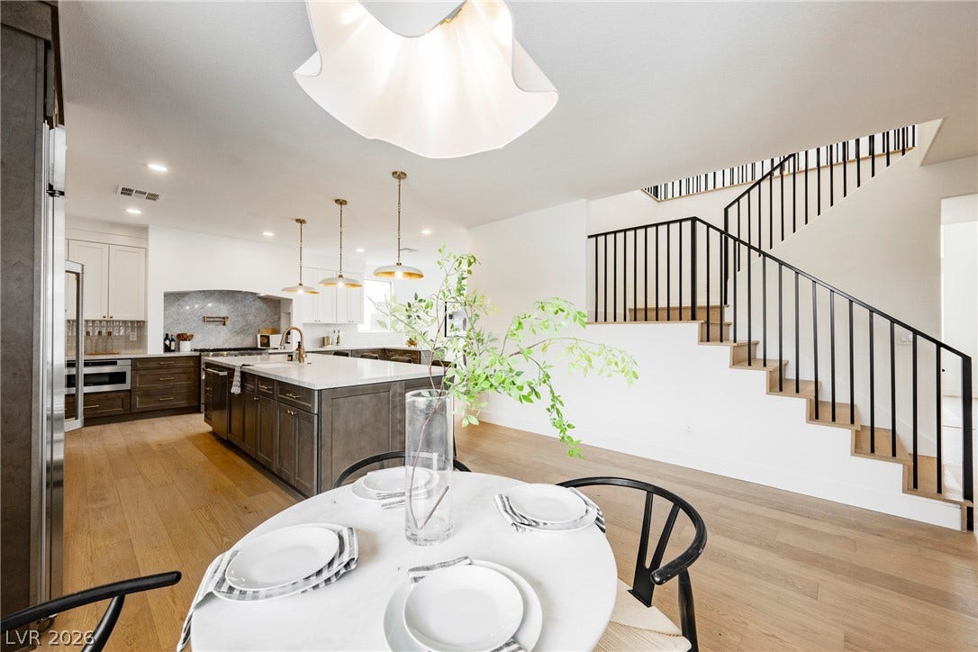 Warm hardwood floors connect a modern kitchen and adjacent dining area with sleek stairs.