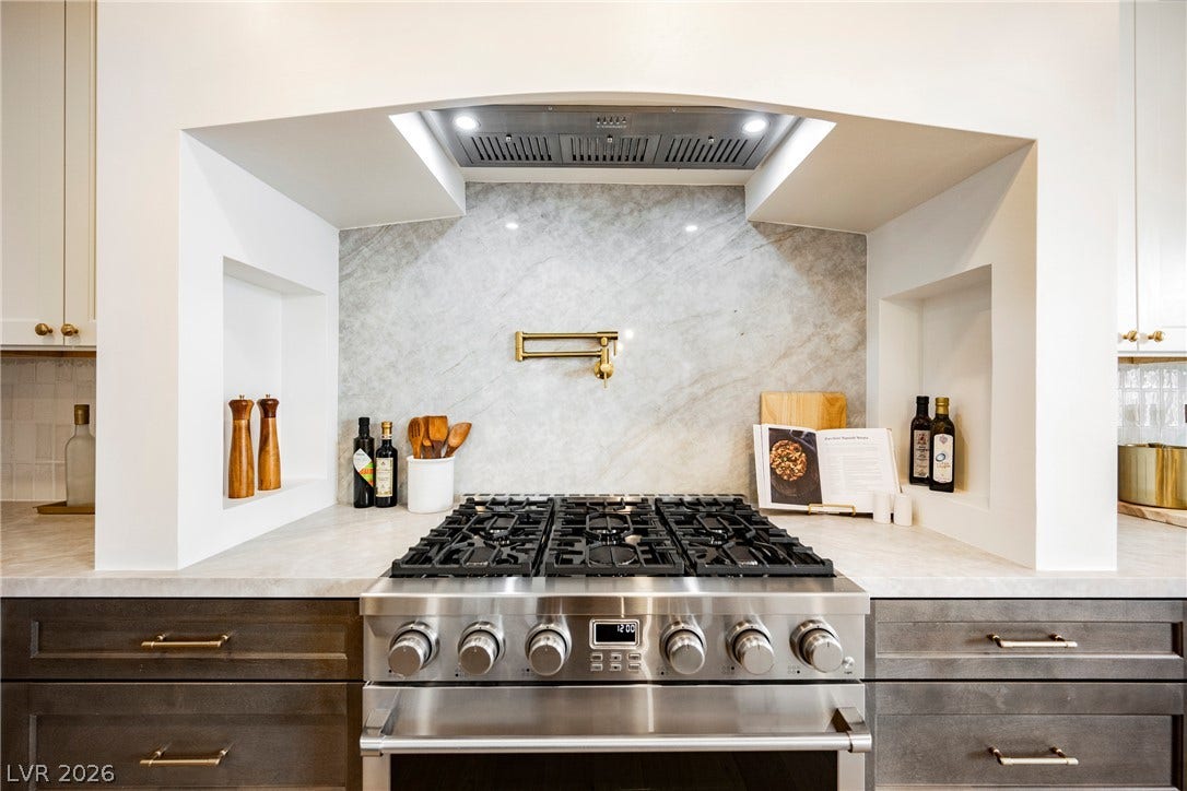 An elegant gas range anchors this custom kitchen cooking alcove complete with marble slab details.