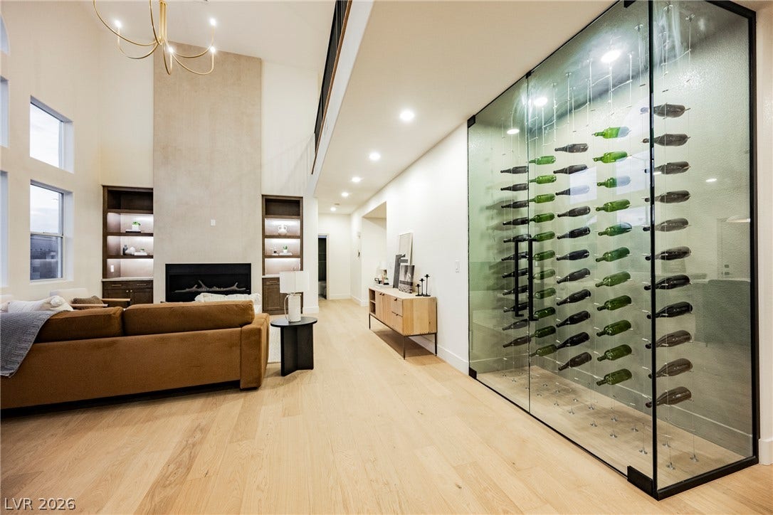 Vaulted ceilings and wide-plank wood flooring frame a modern fireplace and custom glass wine display.