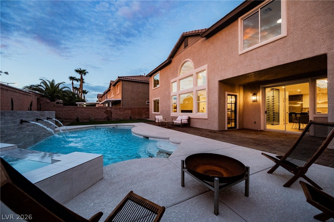 An inviting backyard oasis features a glistening pool paired with a sleek modern fireplace.