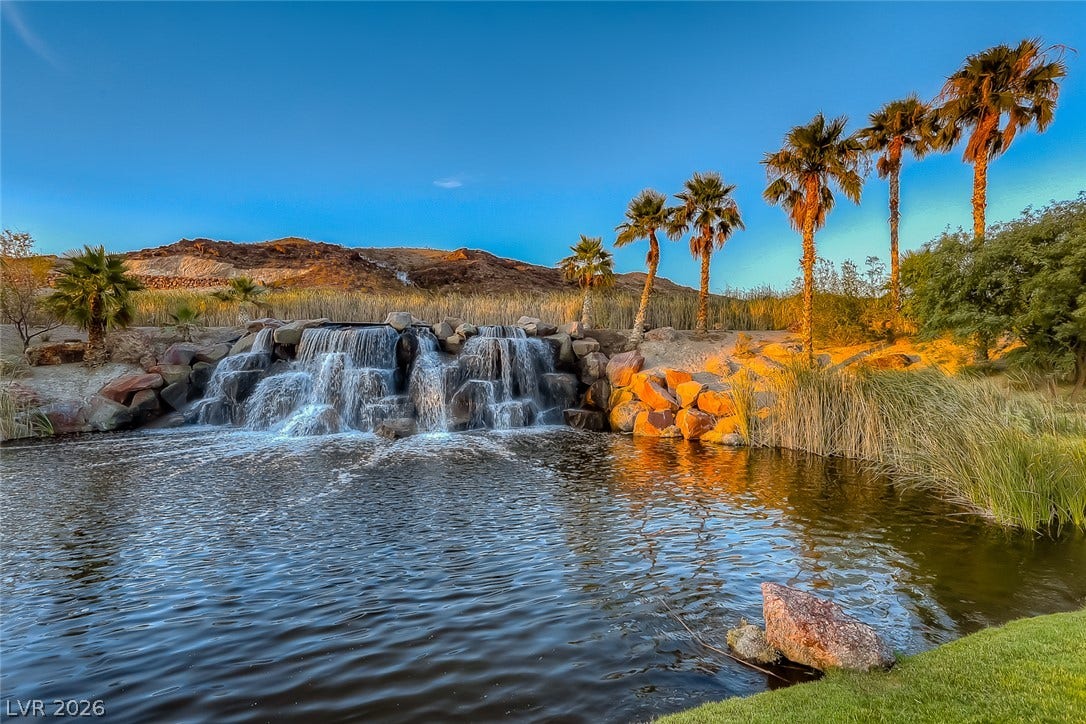 30 Sand Star Lane, Henderson, NV 89011 A cascading rock waterfall feeds into a serene pond framed by towering palm trees.