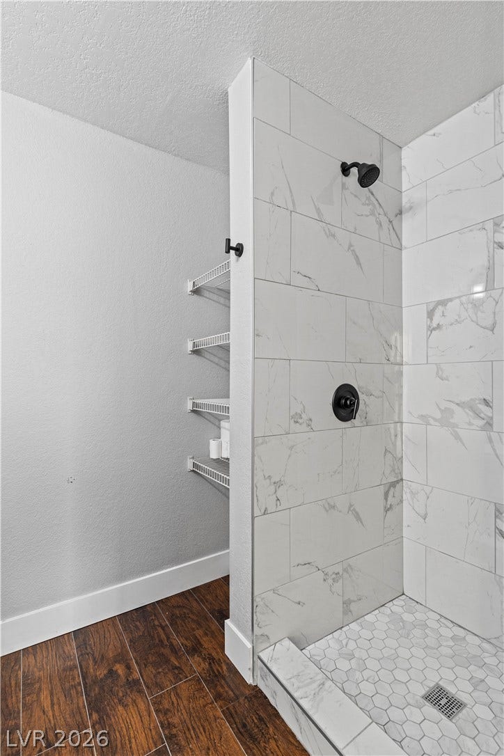 Rich wood-look flooring contrasts beautifully with classic marble-patterned shower tiling.