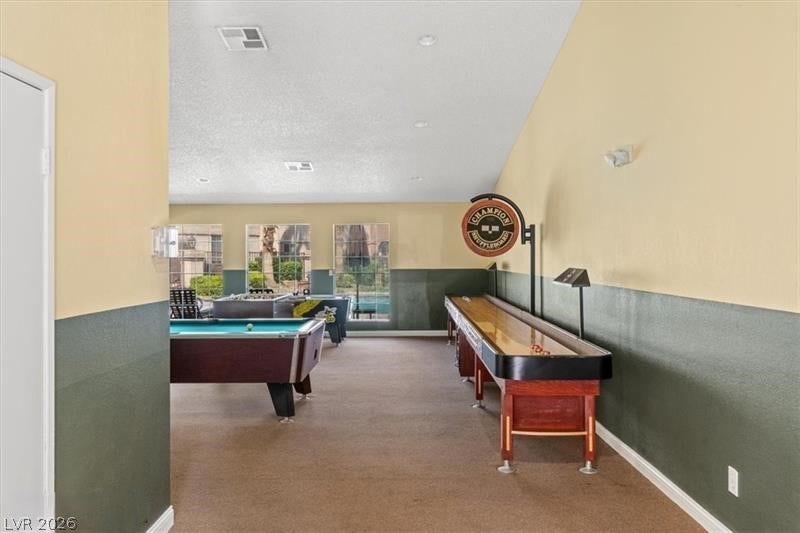 A spacious recreation room features vaulted ceilings, recessed lighting, and large windows overlooking the outdoor pool.