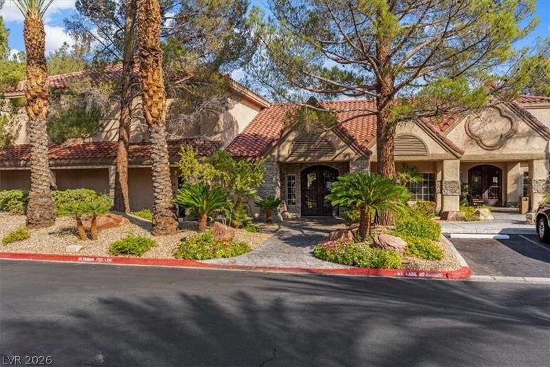 Mature trees and desert landscaping frame the classic tile-roofed entrance of this elegant clubhouse.
