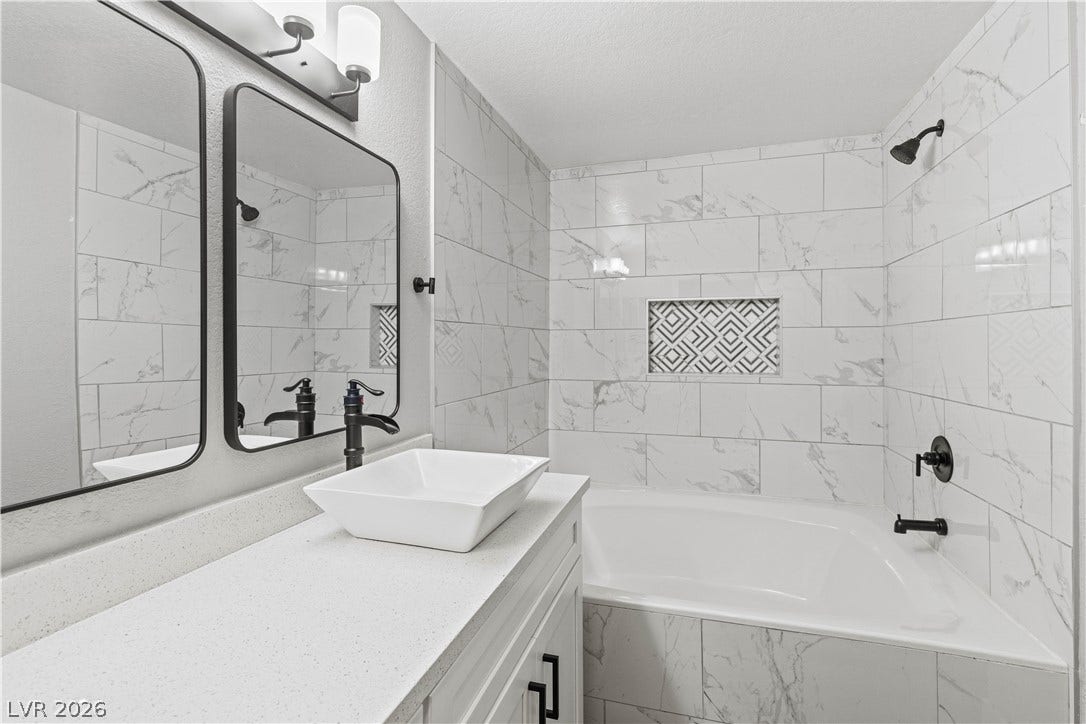 Gleaming stone counters pair elegantly with classic marble-look tiling around the soaking tub.