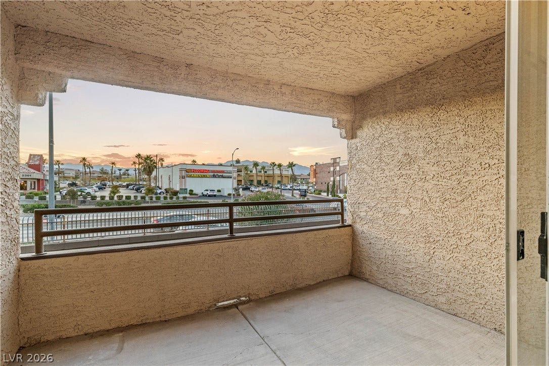 A private covered balcony features textured stucco walls and concrete flooring overlooking the neighborhood.