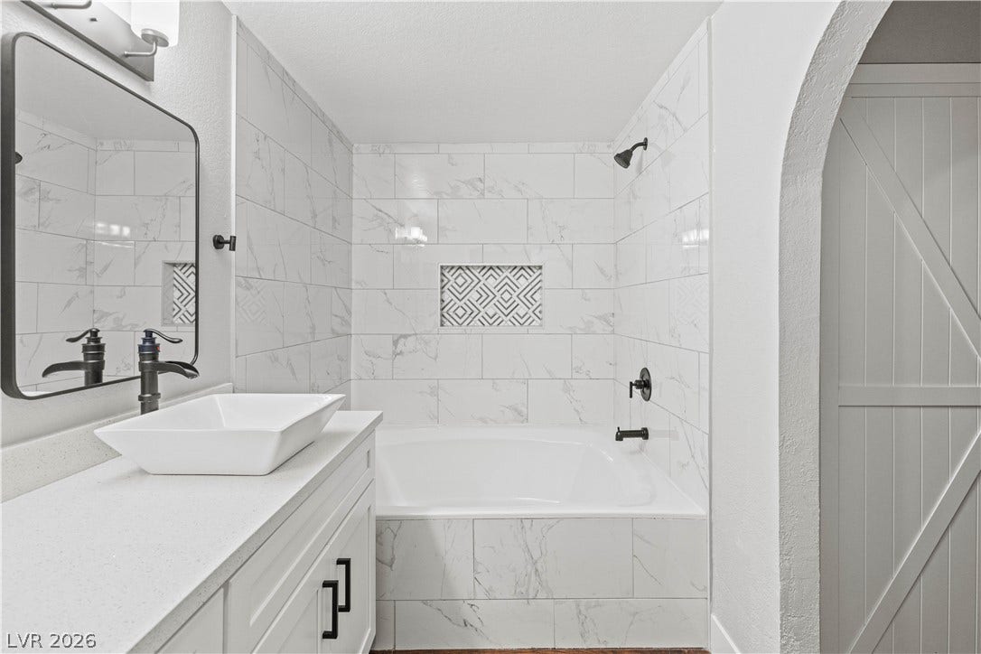 Marble-patterned tile surrounds a deep soaking tub paired with a modern vessel sink vanity.