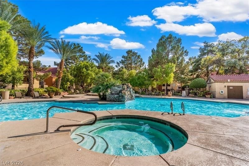 A circular spa sits adjacent to a larger swimming pool surrounded by mature palm trees.