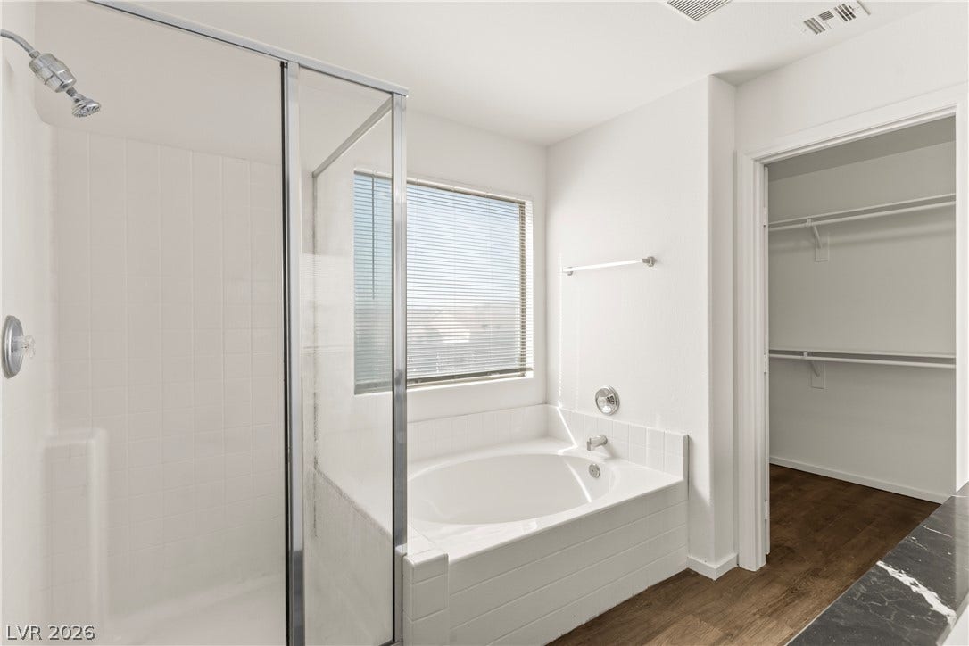 Rich wood flooring anchors this bath containing a glass-enclosed shower and a deep soaking tub.