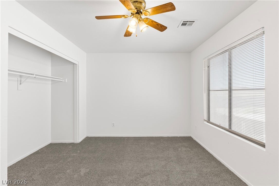 Plush carpeting anchors this versatile room under a smooth ceiling with a wide window.