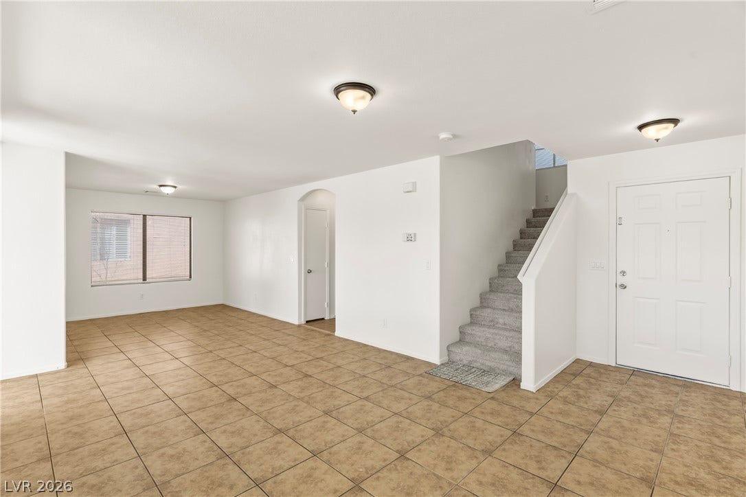 An open living space features durable tile flooring, white walls, and carpeted stairs.