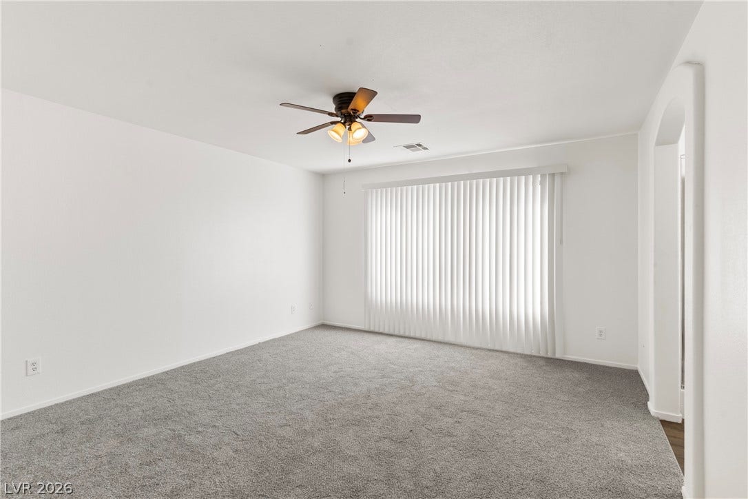An arched doorway opens into a quiet bedroom featuring plush carpeting and a wide window.