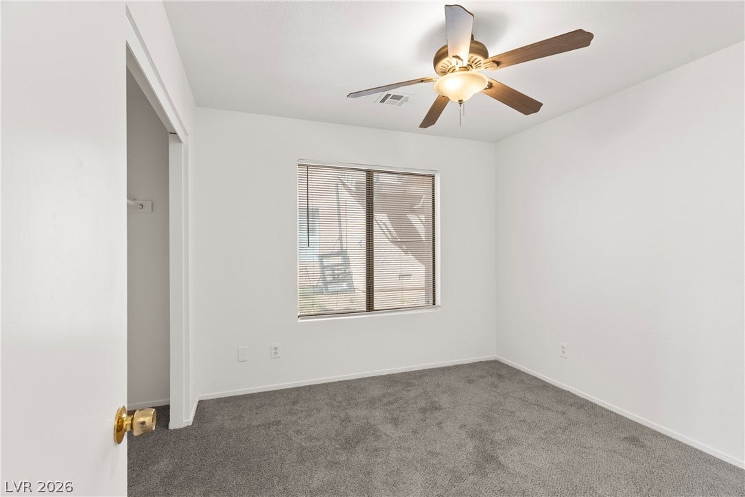 Soft carpeting underfoot anchors this quiet bedroom filled with natural light from a central window.