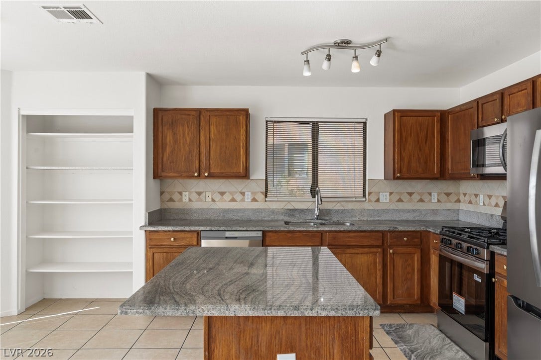 Rich wood cabinetry surrounds a central granite island under modern track lighting.