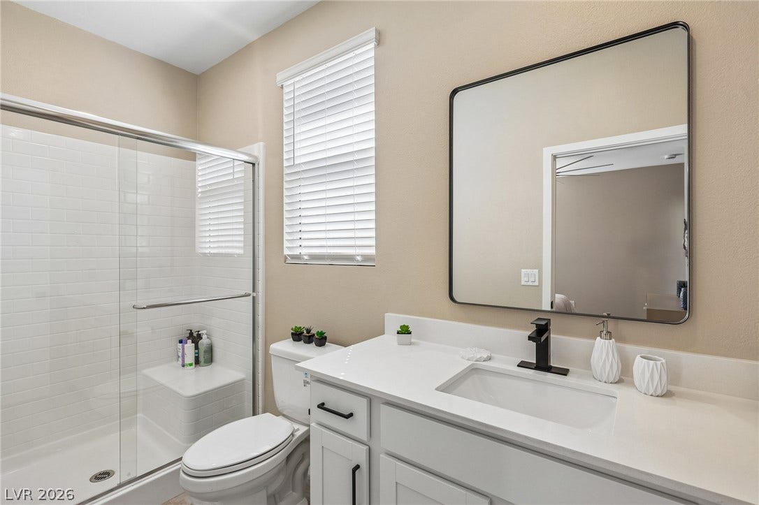 194 Viento Ridge Street, Henderson, NV 89012 A contemporary vanity with stone counters sits adjacent to a glass-enclosed walk-in shower.