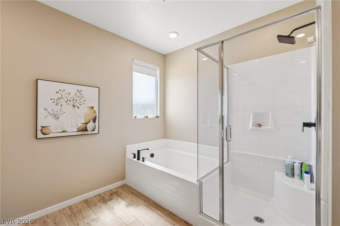 194 Viento Ridge Street, Henderson, NV 89012 A glass-enclosed walk-in shower stands beside a deep soaking tub in this tiled space.