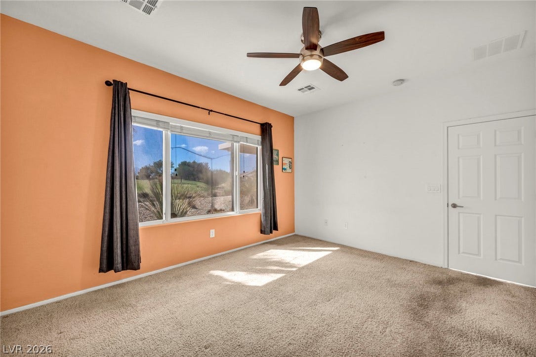 A wide picture window frames views of the golf course from this carpeted bedroom.