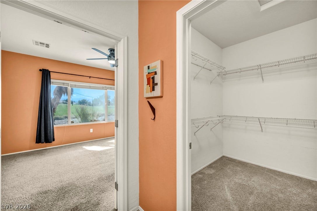 A spacious walk-in closet with built-in wire shelving sits adjacent to a carpeted bedroom.