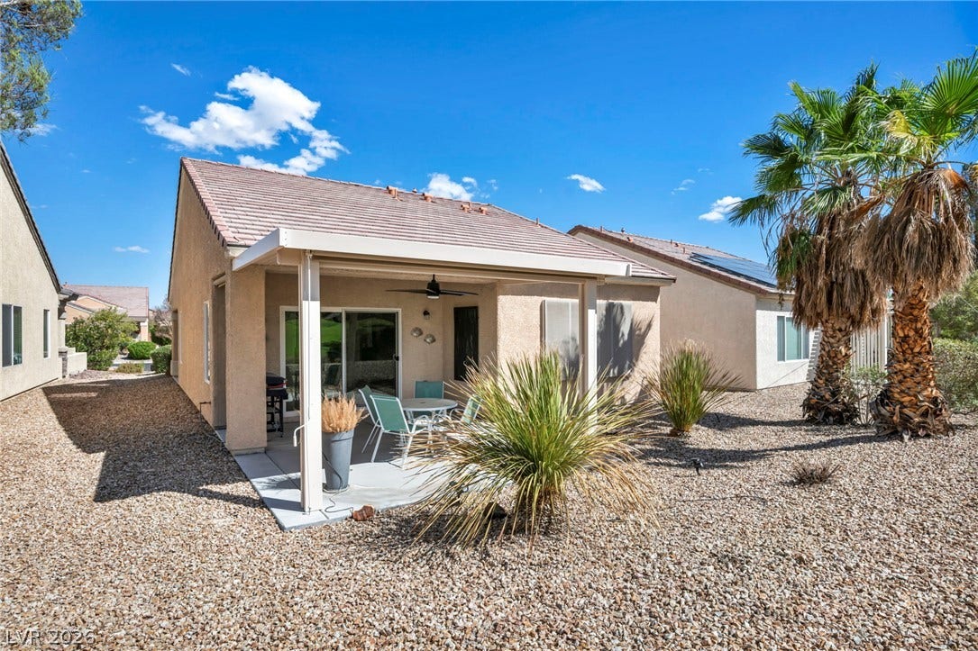 A covered concrete patio overlooks low-maintenance desert landscaping and mature palm trees.