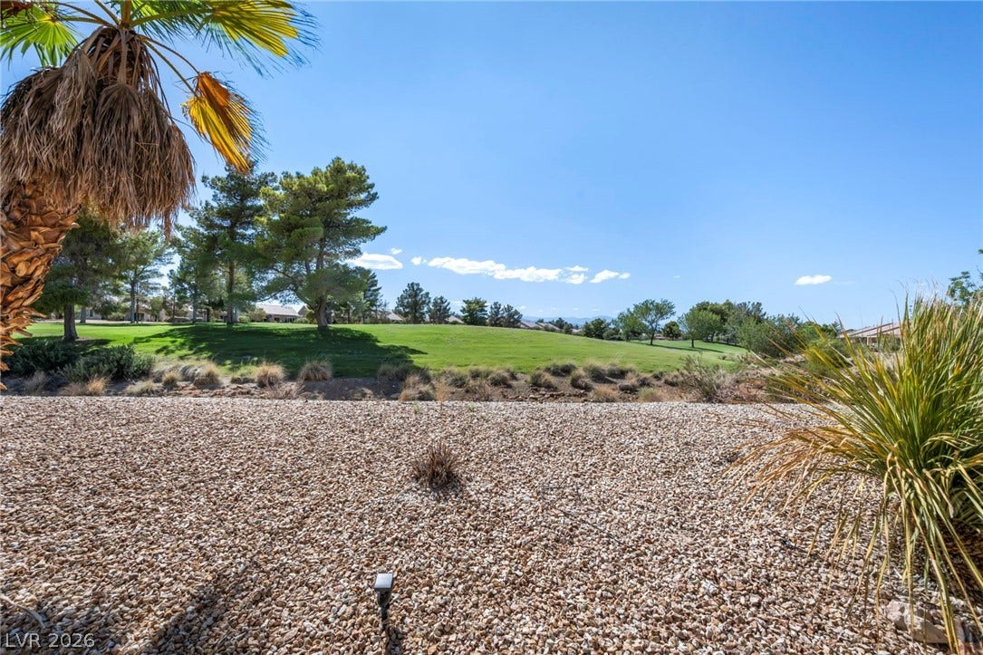 Lush fairways and mature trees border the gravel landscaping under a clear sky.