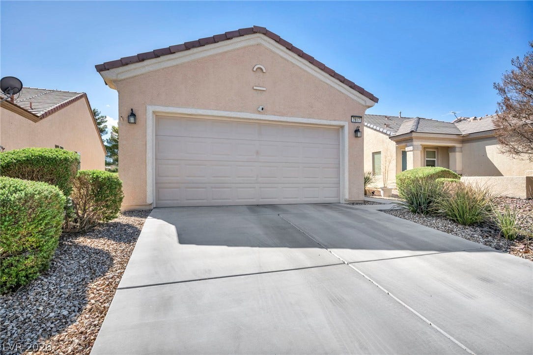 A spacious concrete driveway leads to a two-car garage under a clear blue sky.