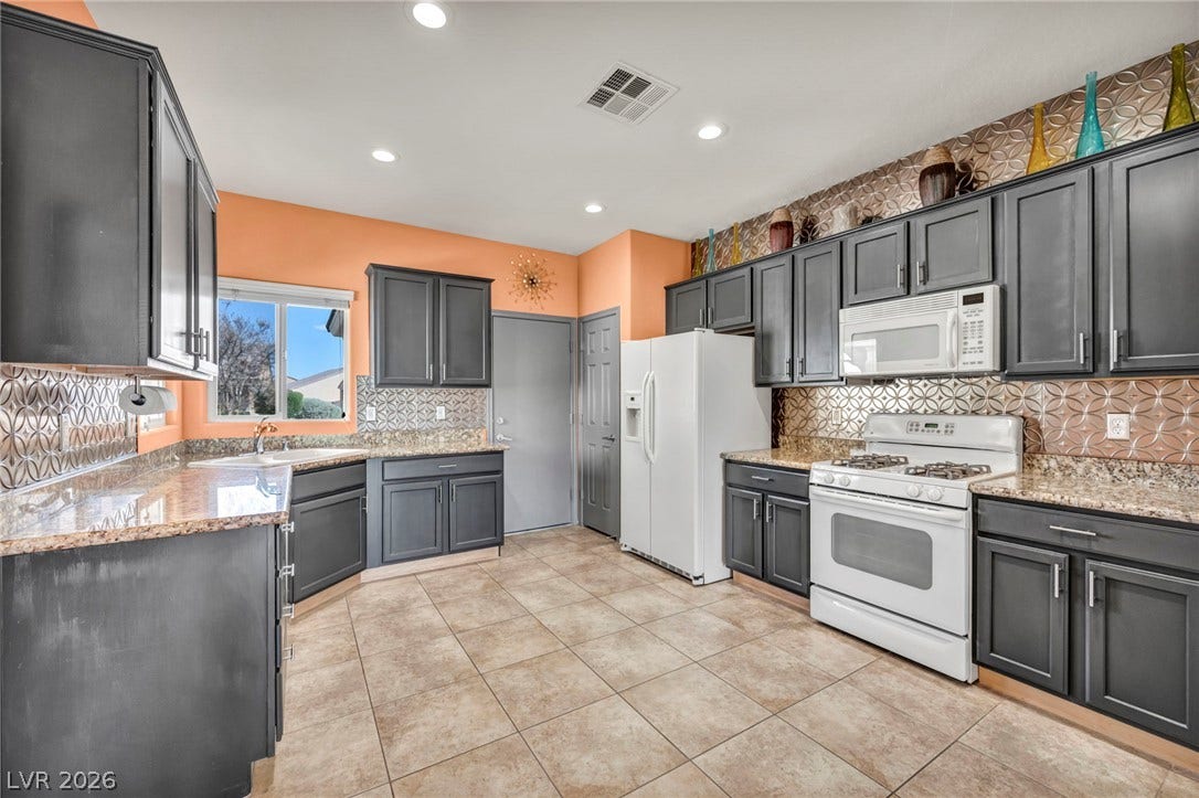Granite countertops and decorative tile backsplashes highlight this spacious kitchen with textured tile flooring.