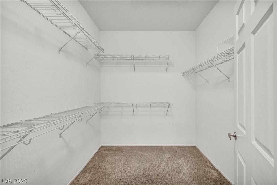 Ample wire shelving lines this functional walk-in closet featuring wall-to-wall carpeting.