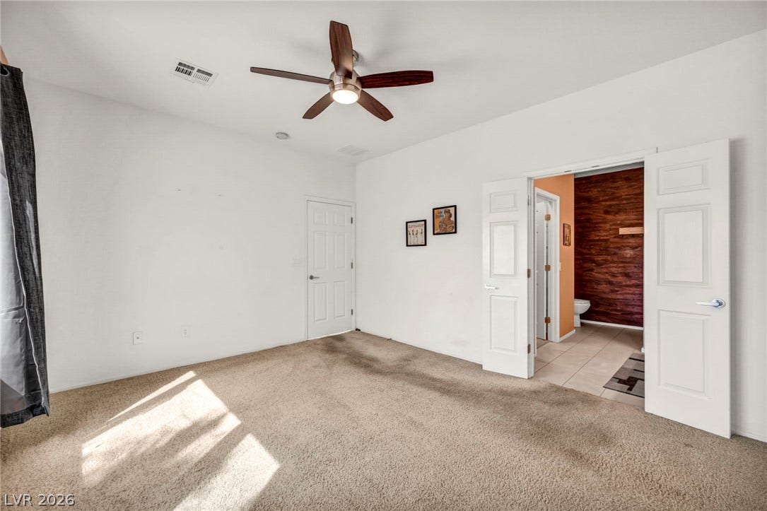 A spacious bedroom features soft carpeting, high ceilings, and an adjoining private bathroom.