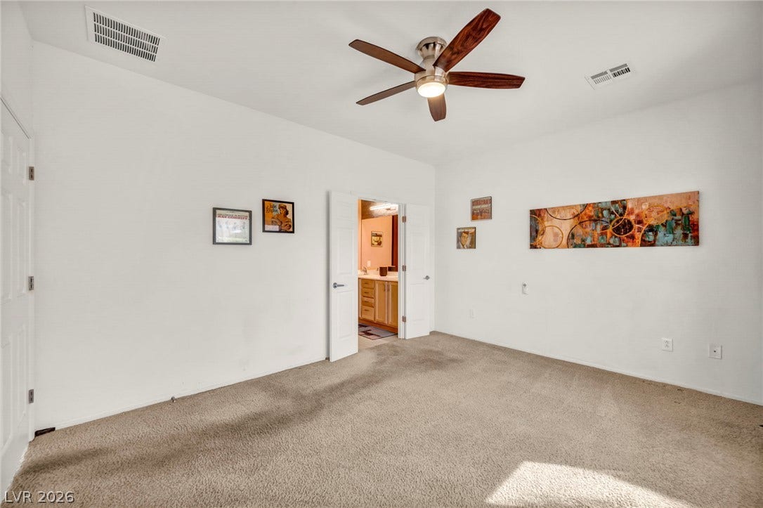 A spacious bedroom features neutral-toned carpeting under a high ceiling.