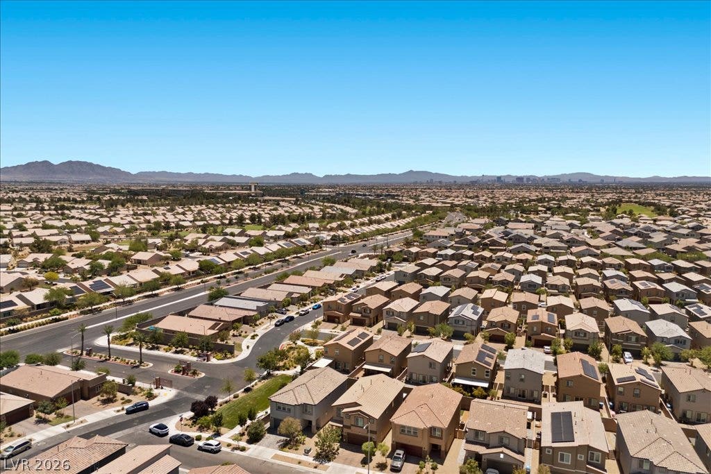 An aerial panorama reveals a vast residential community with distant mountain and city views.